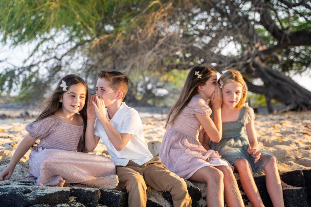children telling secrets on hawaii beach, showing poses for hawaii family portraits