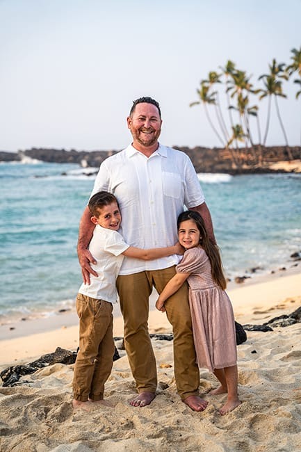 Mother and daughters stand close, hugging each other for Hawaiian family portraits.