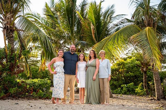 Family of four standing together under palm trees during a Hawaii family photo session on a tropical beach.