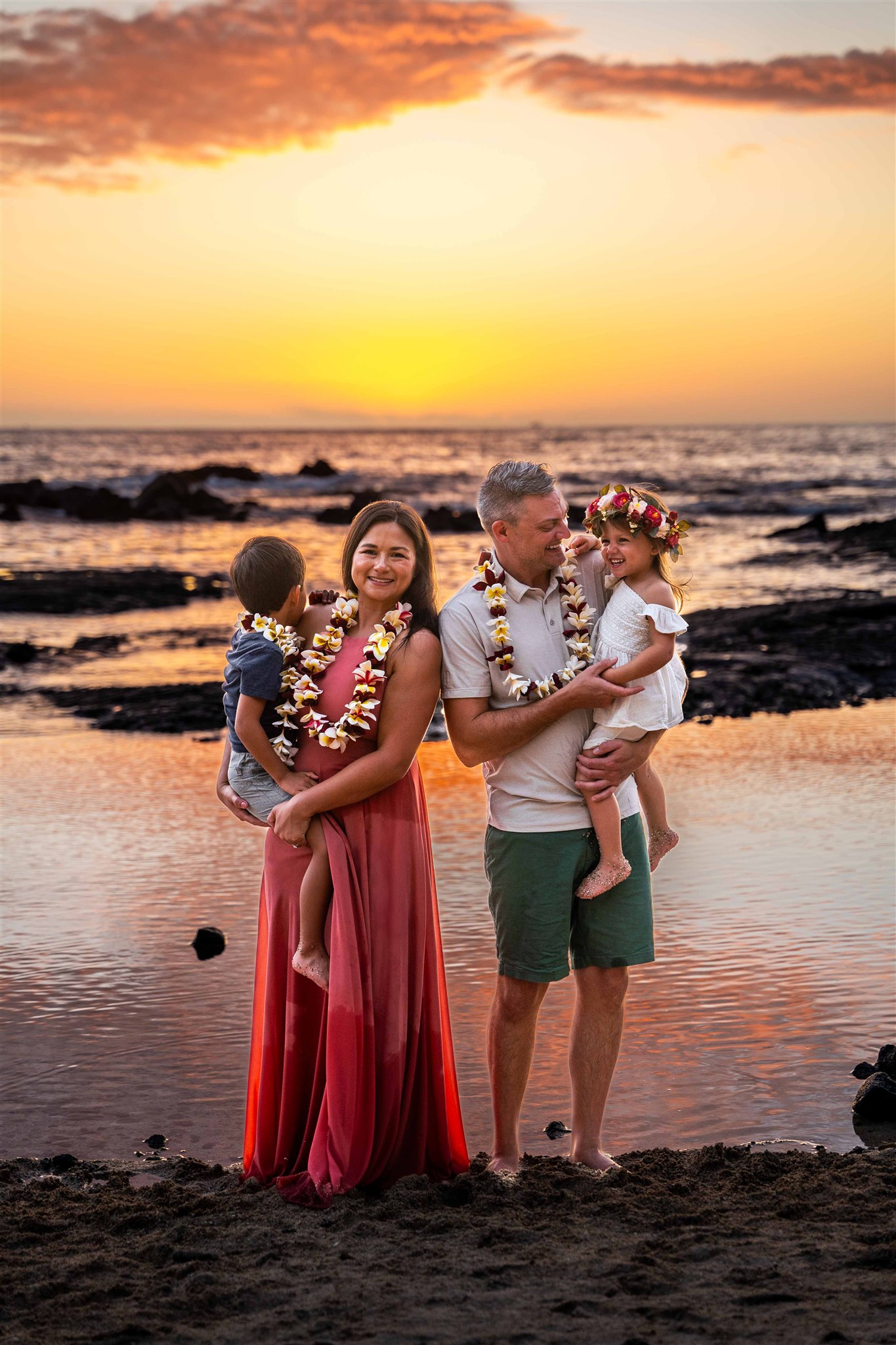 Parents hold their children in front of the beach during sunset for a Hawaii family photoshoot.