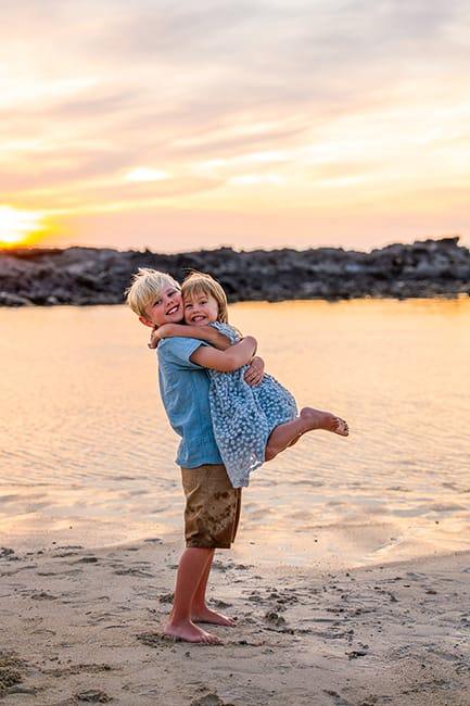 Young boy lifting his sister during a Hawaii family photo session at sunset on the beach.