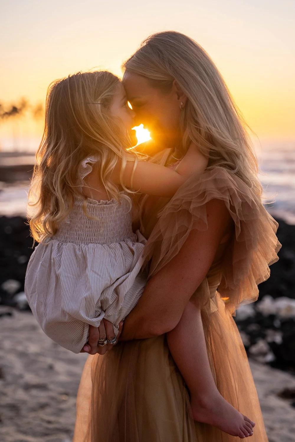 mother holding her little girl during a sunset session at the kona village at a white sandy beach on the big island of hawaii