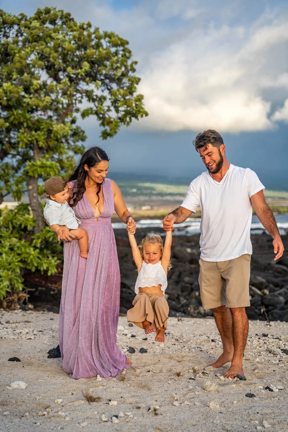 parents swinging little girl on a white sandy beach on the big island of hawaii