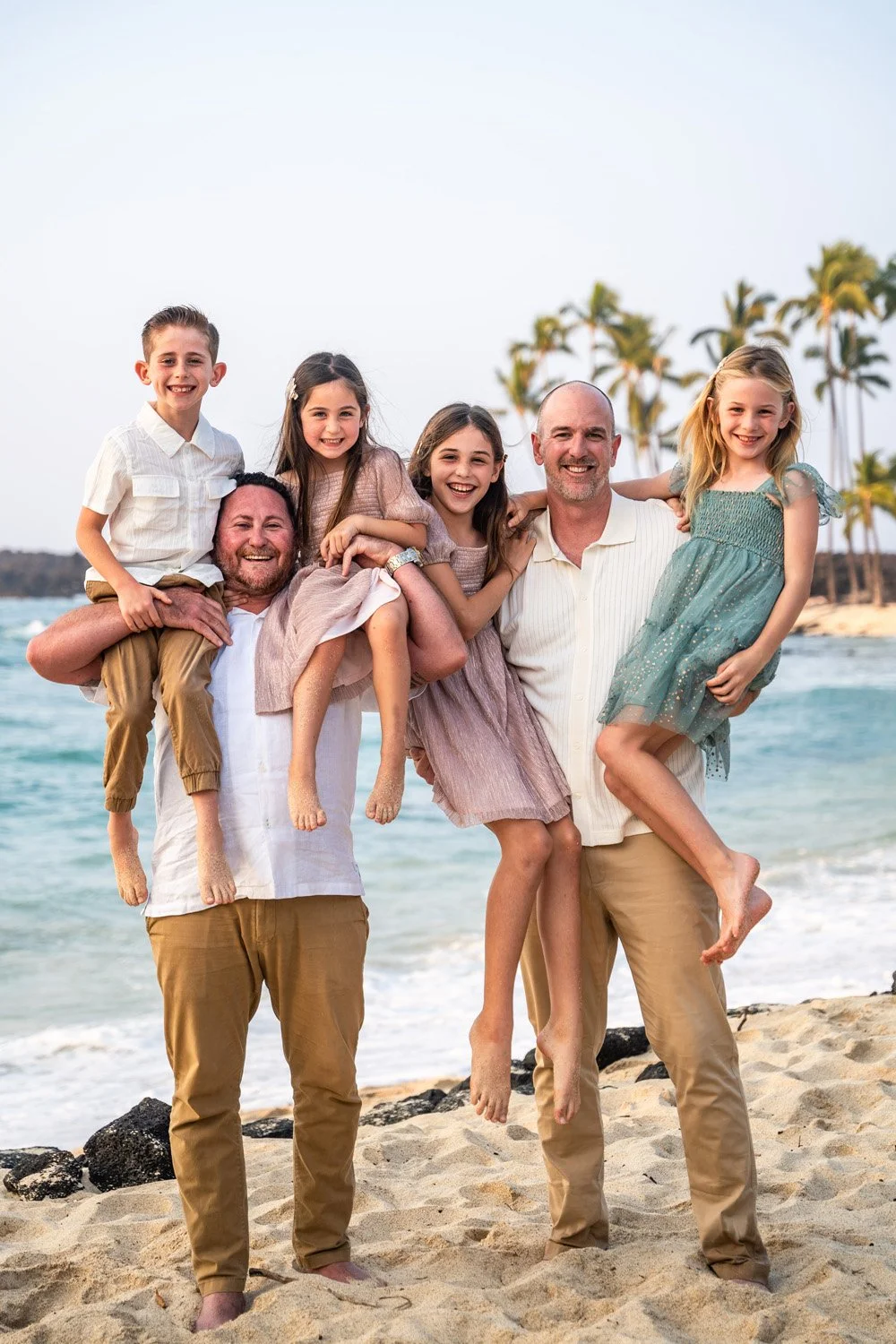 Fathers holding their children on shoulders on a beach in Hawaii