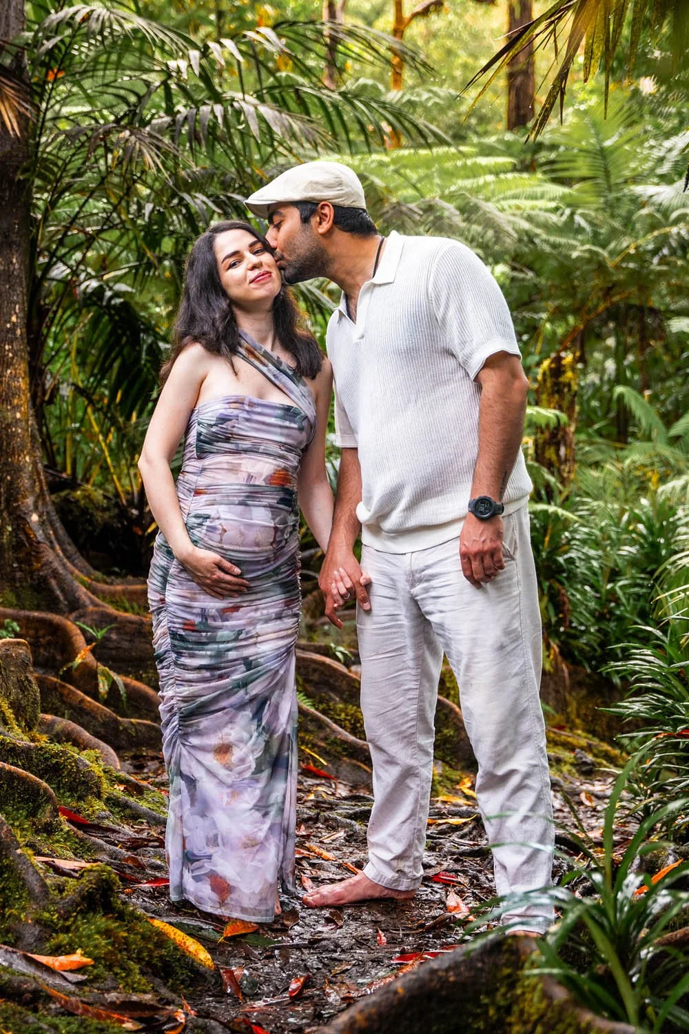 couple holding hands and kissing at the kona cloud forest sanctuary for a maternity baby moon couples portrait session on the Big Island of Hawaii