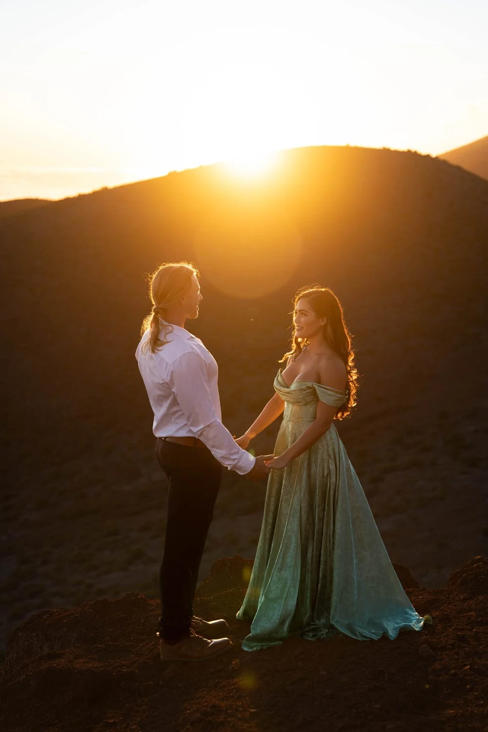 couple holding hands during sunset with a sun flare mountain backdrop for a couples portrait session on the Big Island of Hawaii