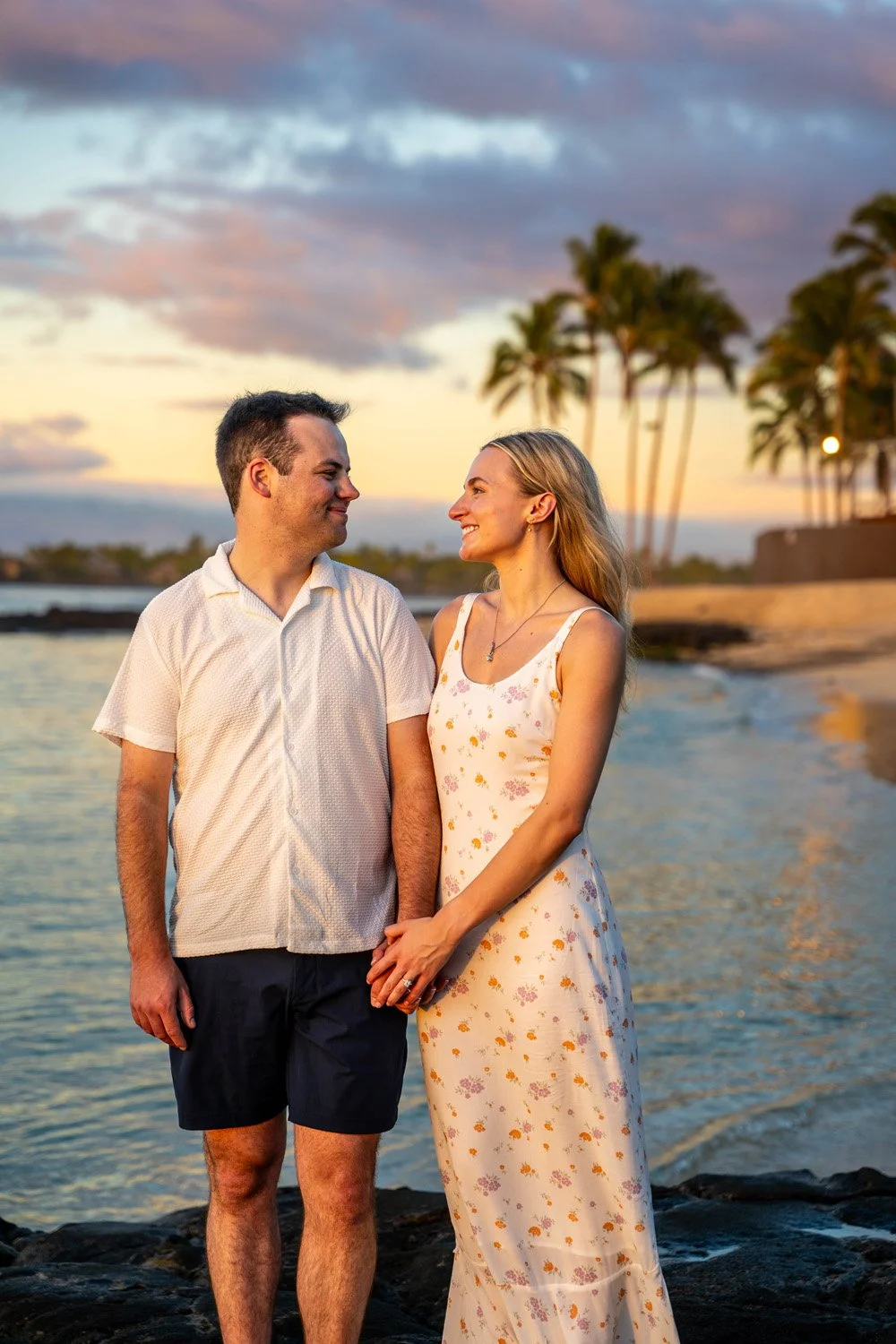 couple holding hands during sunset with palm trees in the background on a white sandy beach at the four seasons hualalai for a couples portrait session on the Big Island of Hawaii