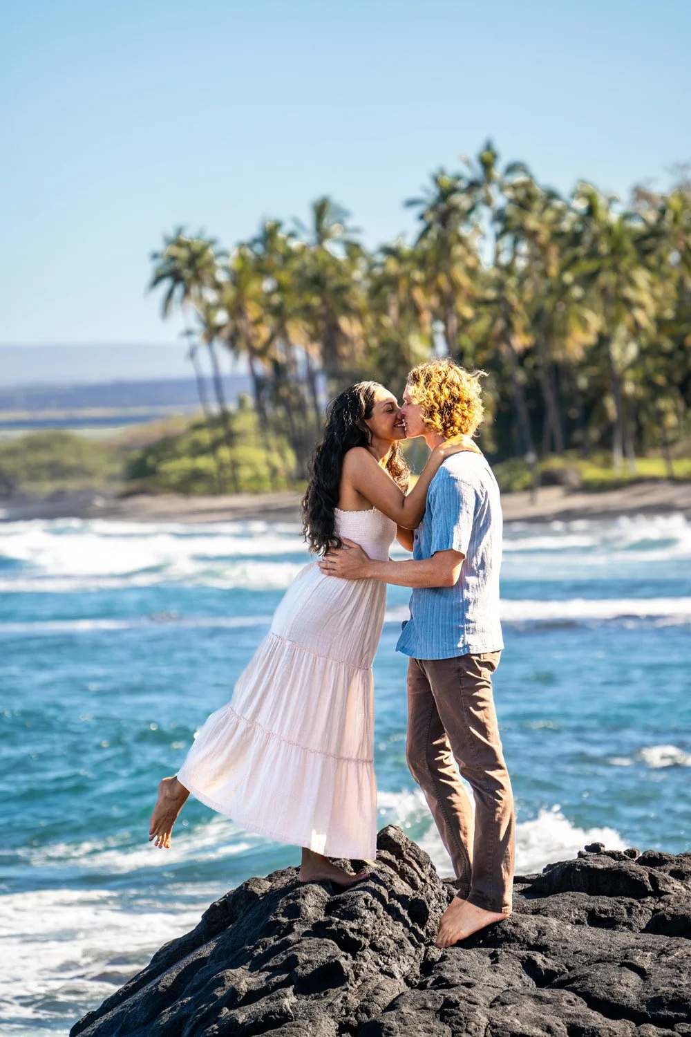 couple kissing on lava rock with palm trees behind them for a couples portrait session on the Big Island of Hawaii