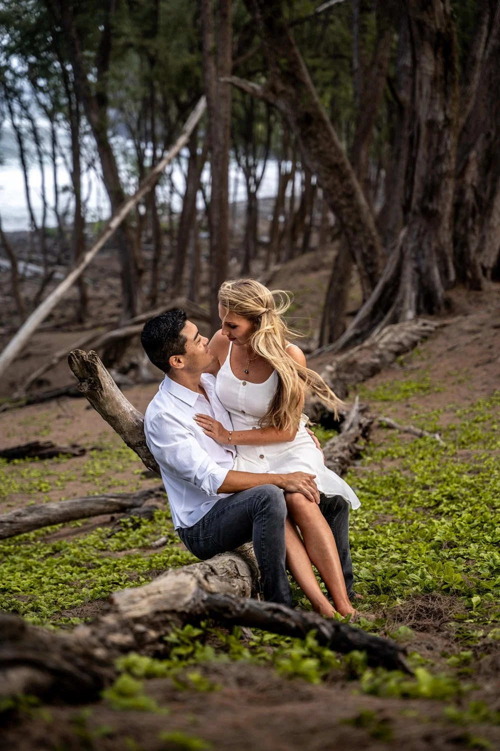 couple sitting in each others lap in a forest for a couples portrait session on the Big Island of Hawaii