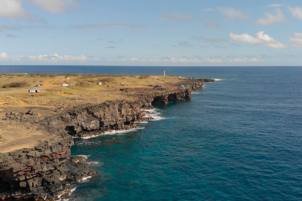 Aerial view of South Point on the Big Island of Hawaii, showing rugged cliffs and turquoise waters during a Volcanoes National Park day trip from Kona.