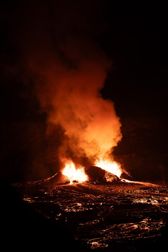 A kilauea erupting at night, with fiery orange lava flowing and thick smoke rising into the dark sky—one of the hawaii volcanoes national park best things to do, as the intense glow illuminates the surrounding landscape.