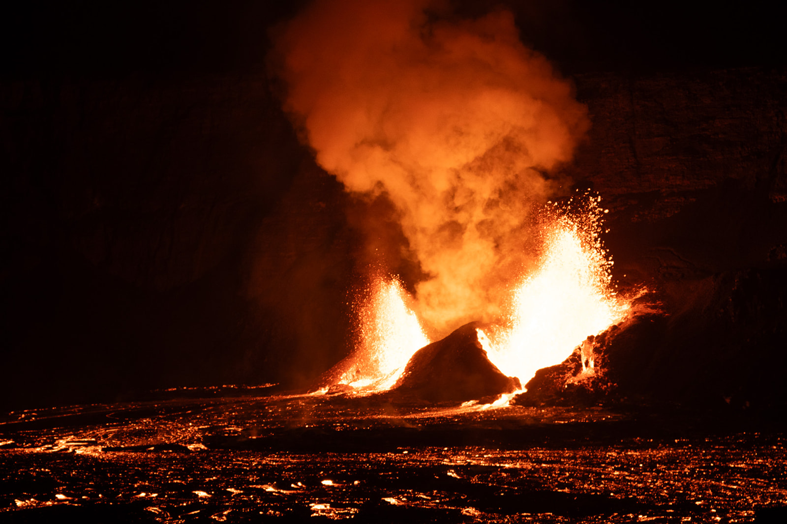 A volcano erupting at night, spewing bright orange lava, smoke, and ash into the dark sky—one of the hawaii volcanoes national park best things to do is witnessing molten lava flowing across the ground around the eruption site.