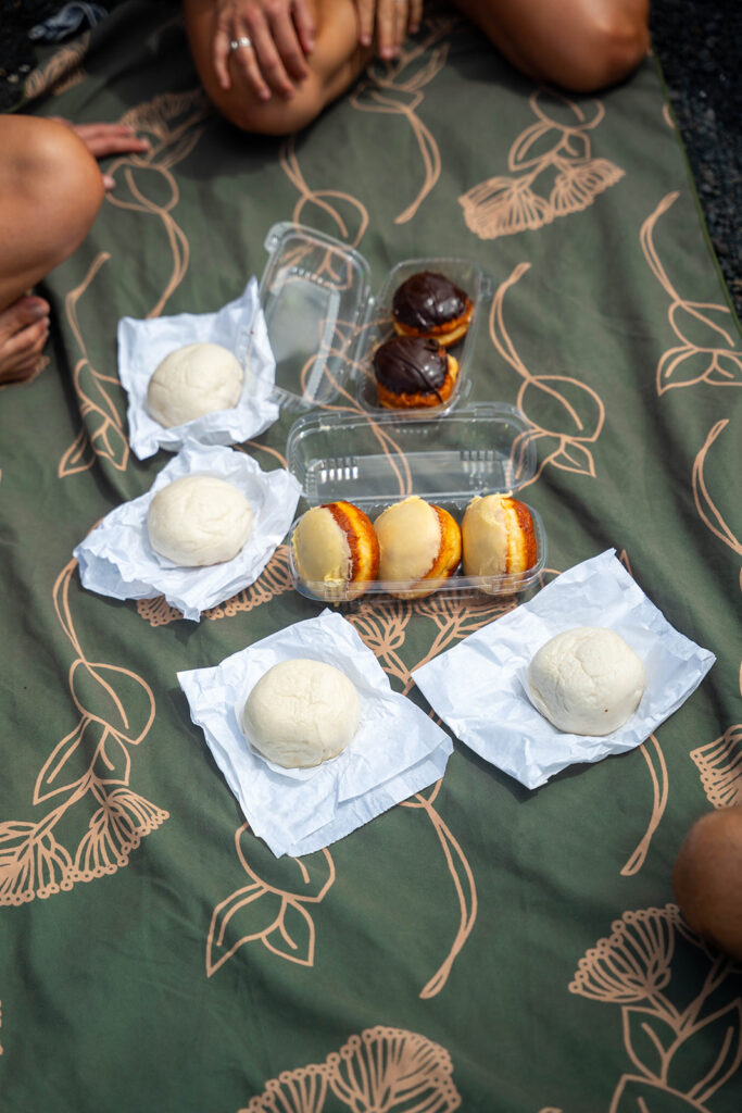 Fresh malasadas and manapua from Punaluʻu Bake Shop laid out for a picnic at Punaluʻu Black Sand Beach on the Big Island of Hawaii.