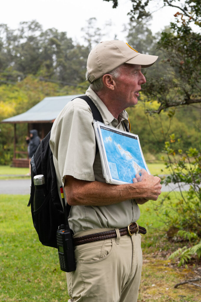 Park ranger leading a guided hike on the Halema‘uma‘u Trail in Hawaii Volcanoes National Park holding a map and sharing insights.