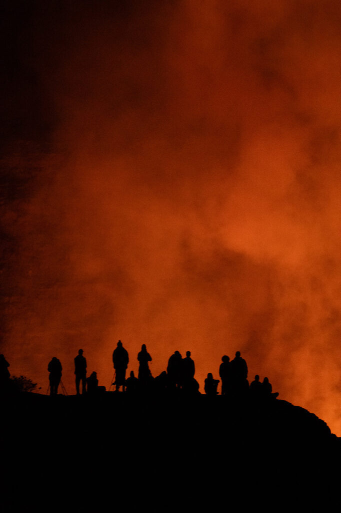 Silhouettes of people stand on Halemaʻumaʻu Crater ridge looking at Kīlauea eruption, capturing the intensity often seen at Hawaii Volcanoes National Park—one of the best things to do for nature and adventure lovers.