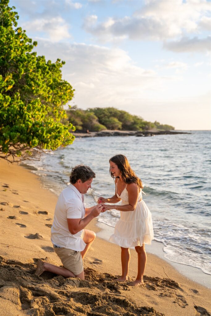 Man placing engagement ring on his partner&rsquo;s finger during a sunset beach proposal in Waikoloa, Big Island Hawaii