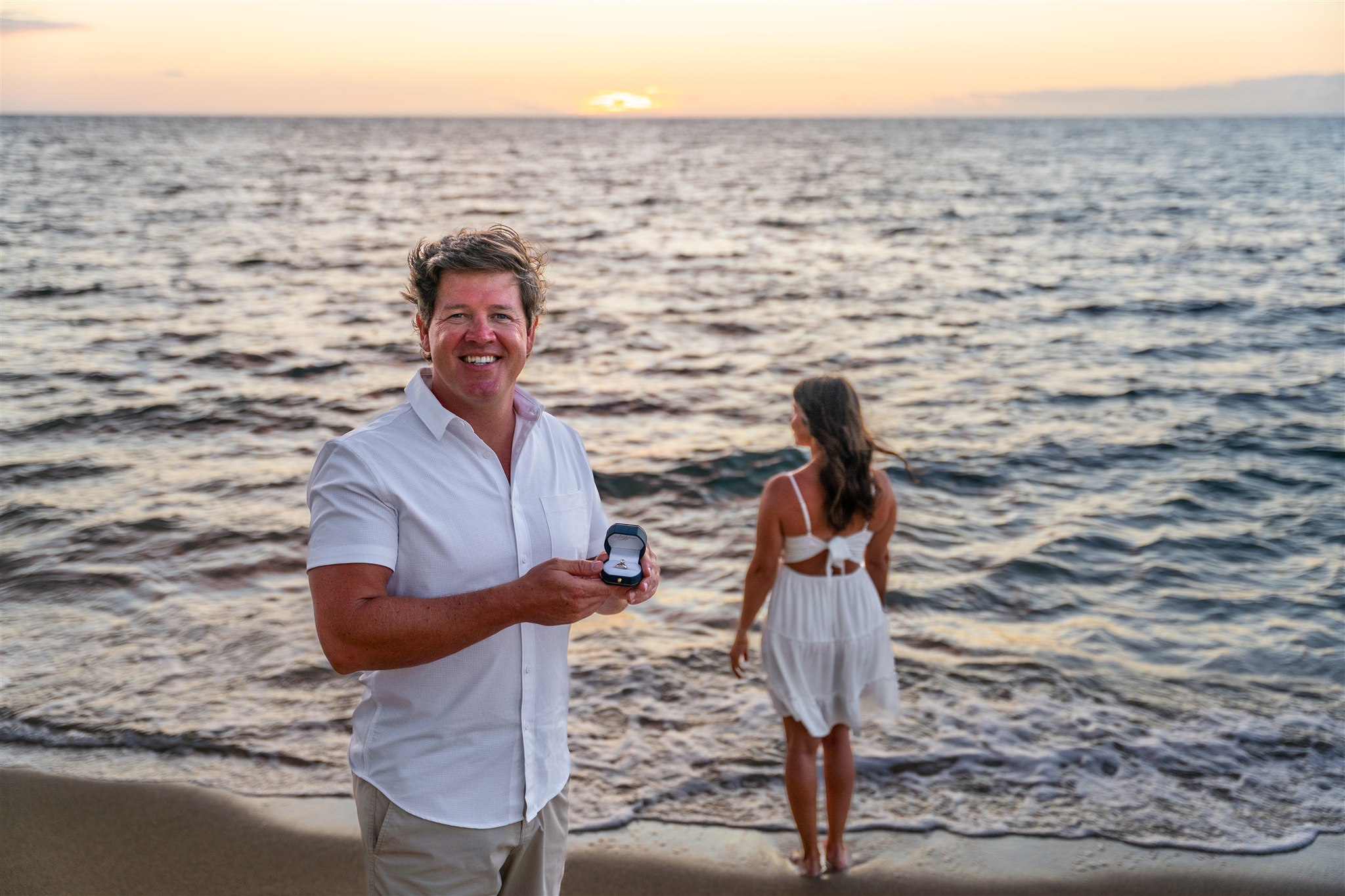 man holding engagement ring during sunset proposal at ʻanaehoʻomalu beach in waikoloa on the big island of hawaii