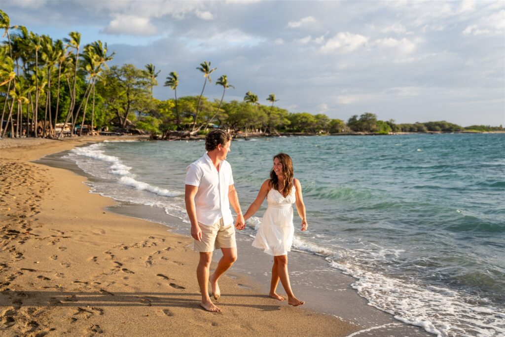 Couple walking hand in hand along the shoreline during a Waikoloa Beach proposal at Anaehoʻomalu Bay, Big Island Hawaii
