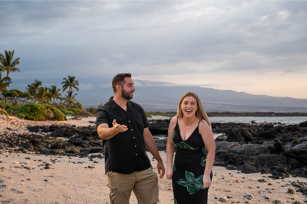 Couple laughing together during a surprise beach proposal at sunset on the Big Island of Hawaii.