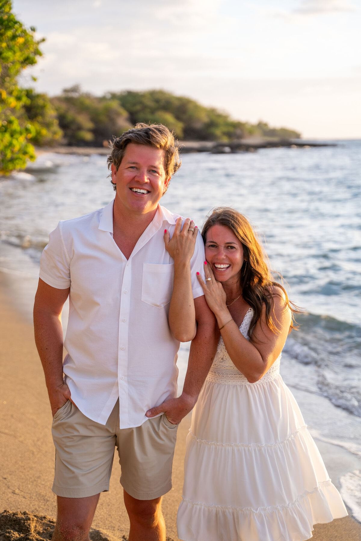 A woman holds onto a man with a smile on their face during engagement photos in Hawaii.