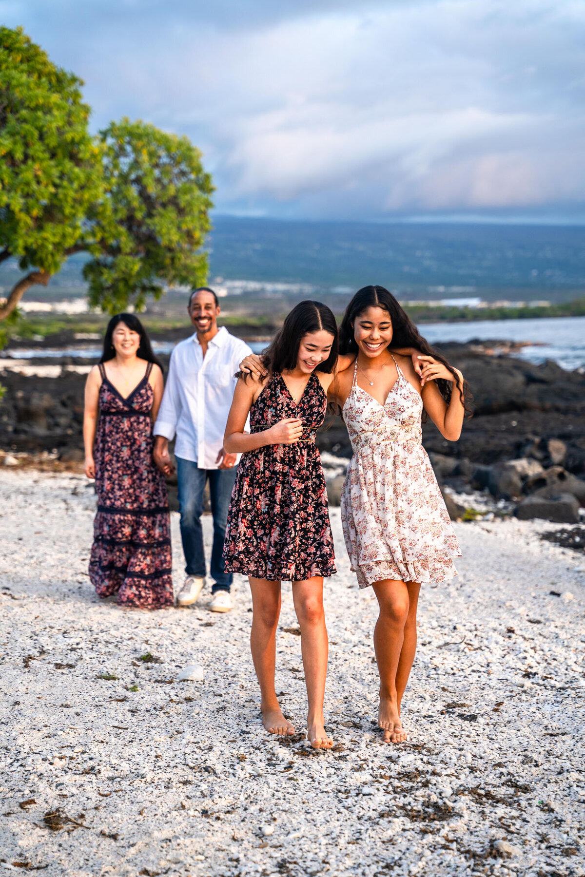 Daughters walking together on the beach with their parents behind them in Hawaii.