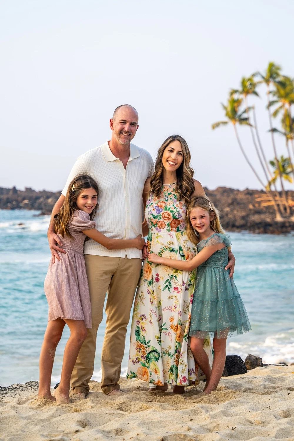 Parents and their two daughters standing together during a Hawaii family photo session by the ocean.