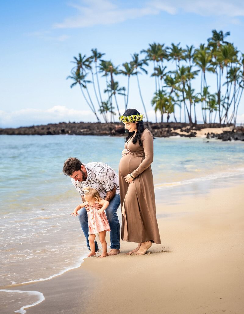 Pregnant mother standing with her husband and child on a beach during a Hawaii family photo session.