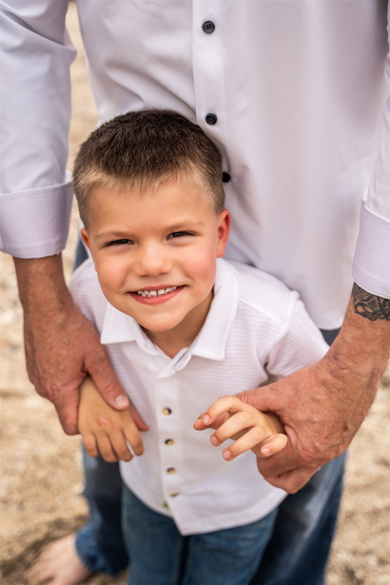 Dad holding son's hands during Hawaii vacation photos with the beach in the background.