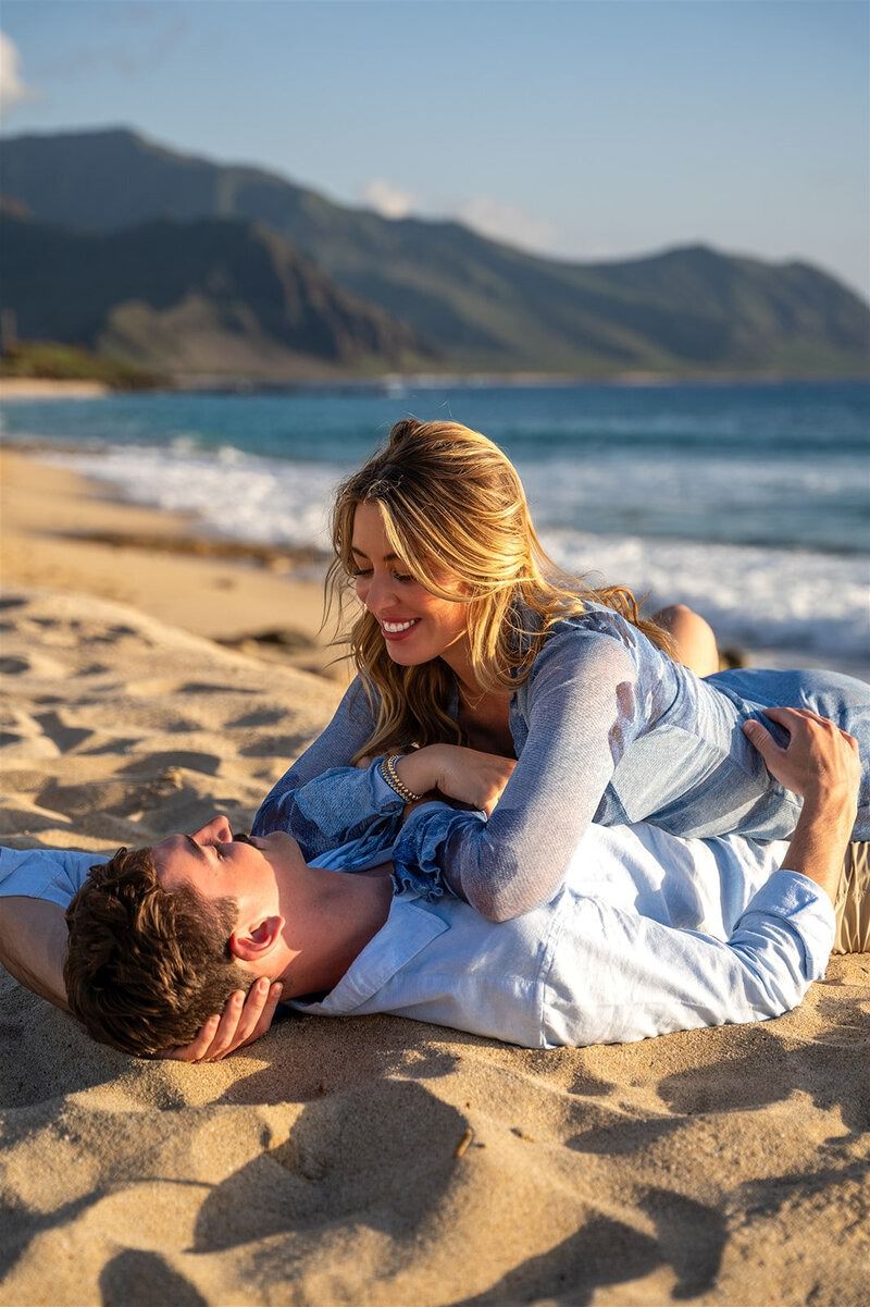 Couple lying together on the beach during a romantic engagement photo session.
