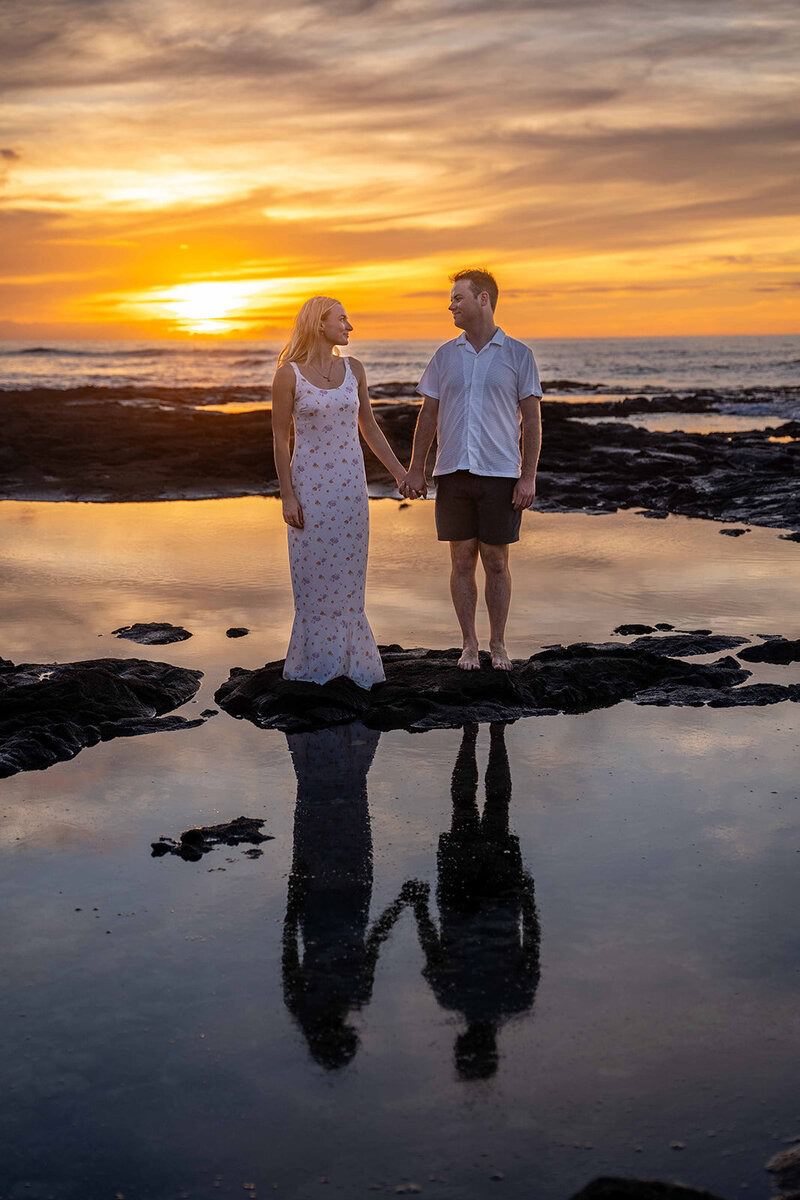 Couple stands hand-in-hand with the sunset behind them during engagement photos.