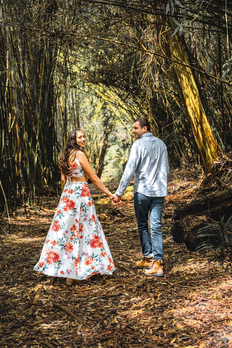 Woman in a floral dress holding hands with her partner during tropical engagement photos.