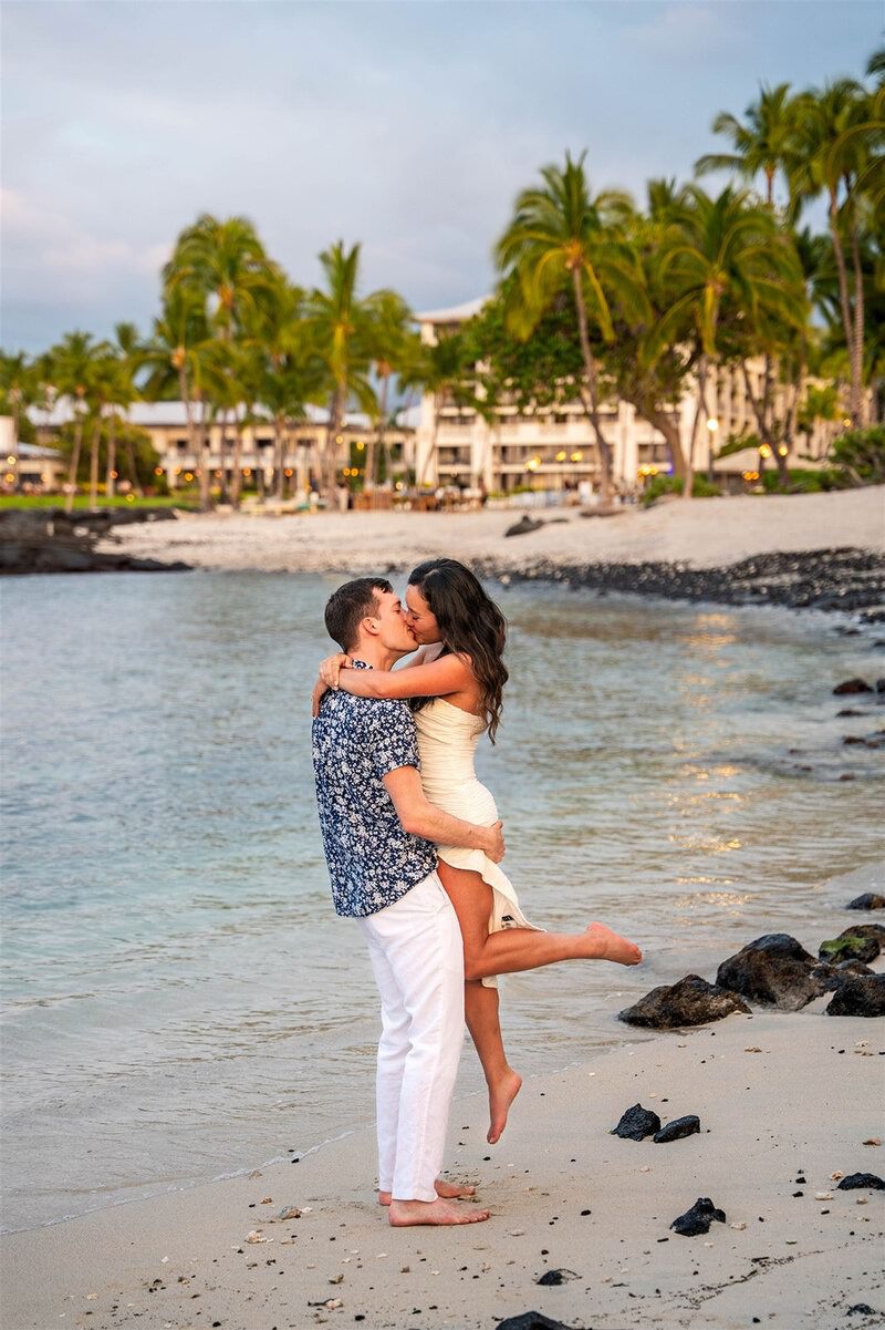 Man picked up the woman with her foot in the air during engagement photos on the beach.
