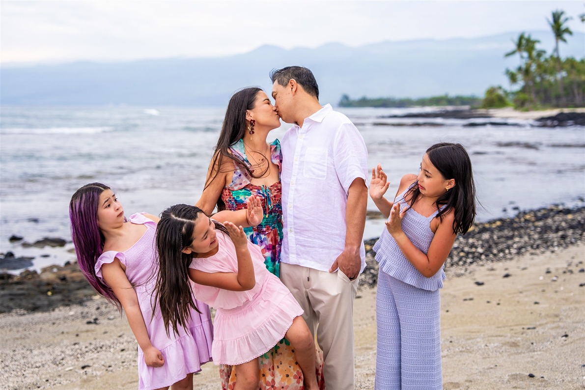 hawaii family photo of the mom and dad kissing and the girls looking away